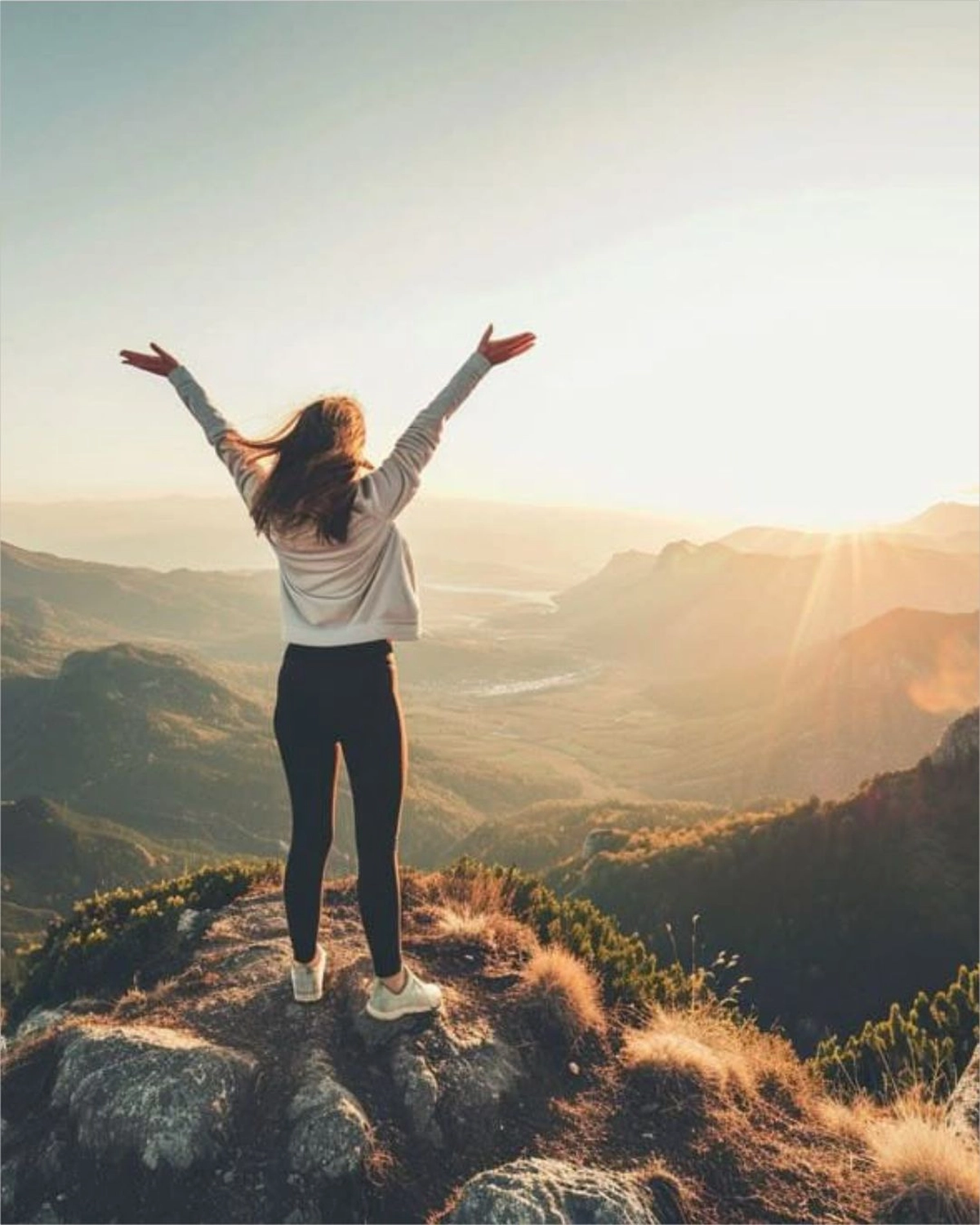 Sirima Miller – LEBENS(T)RAUM für Körper, Geist & Seele – eine Frau, die bei Sonnenaufgang triumphierend auf einem schroffen Berggipfel steht.